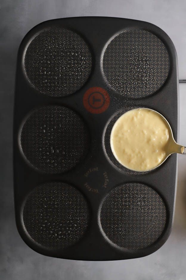 Batter poured with a ladle into the six round wells of a pancake pan for fluffy pancakes