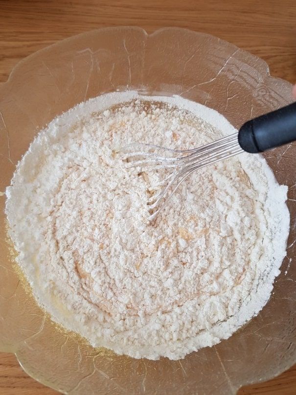 Flour and sugar whisked together in a large glass bowl on a wooden table