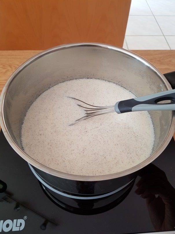 Sugar and milk stirred with a whisk in a steel pot on the induction hob