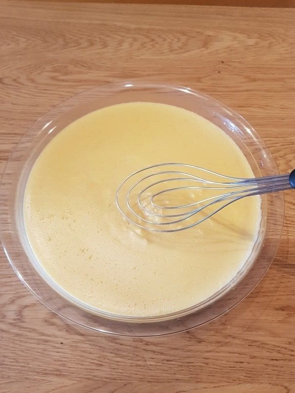 Golden yellow pastry cream whisked smooth in a large glass bowl