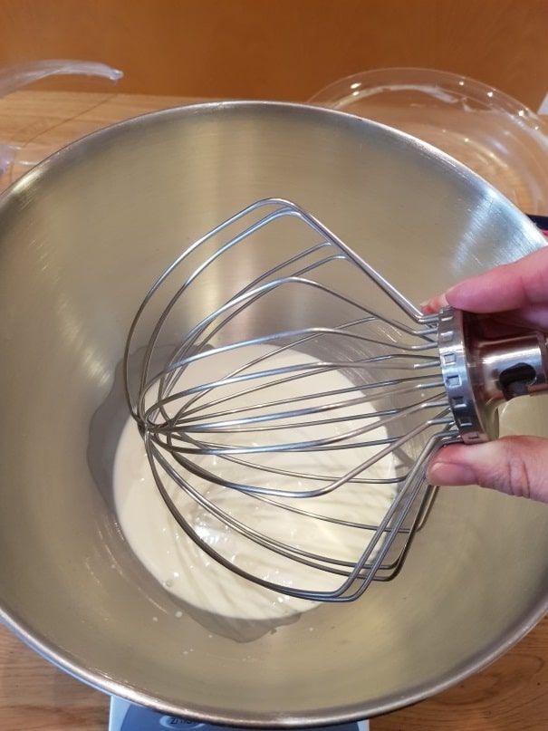 Balloon whisk fitted to the stand mixer with liquid cream waiting in the steel bowl