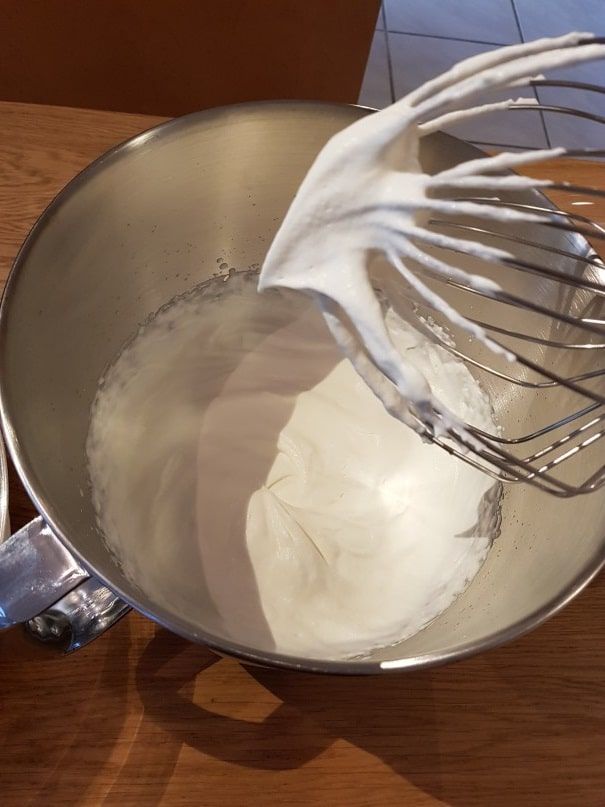 Stiffly whipped cream clinging to the balloon whisk above the stand mixer bowl