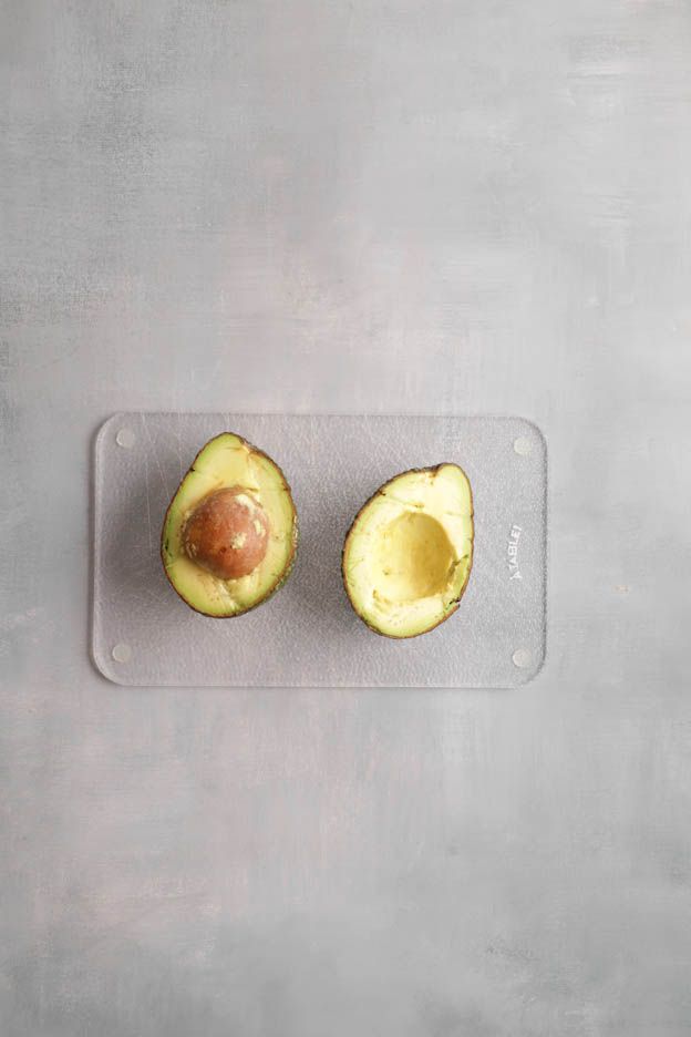 Halved avocado with the stone on a glass cutting board for the brick tartlets