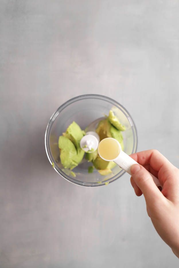 Avocado chunks in a glass bowl with lemon juice being added by spoon for the brick pastry tartlets