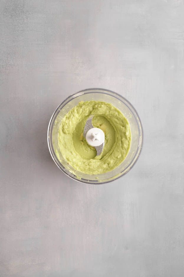Freshly blended avocado purée in the food processor bowl with the blade visible