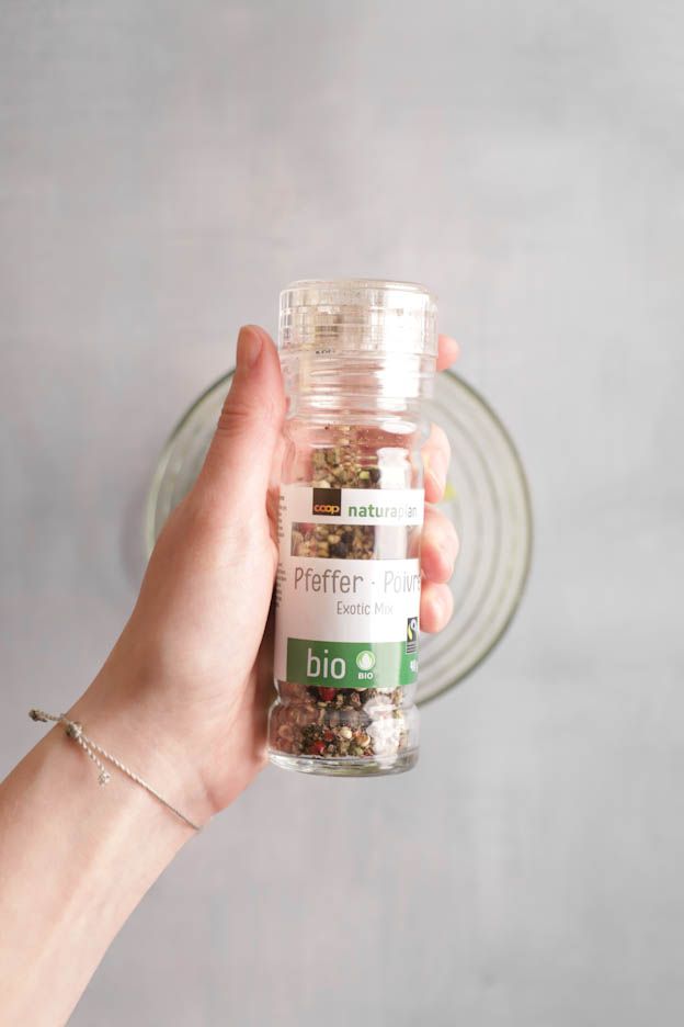 Hand holding an organic spice grinder over the bowl of avocado cream