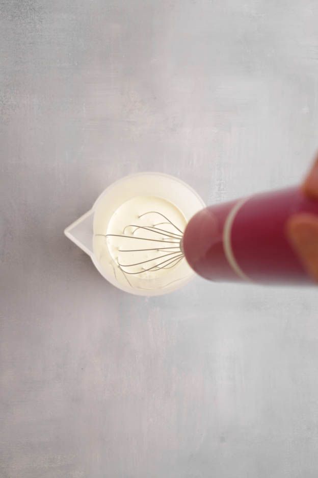 Red handled whisk beating cream in a glass measuring jug for the avocado tartlets