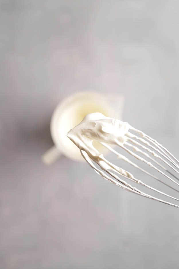 Whisk lifted from the measuring jug with stiffly whipped cream clinging to it