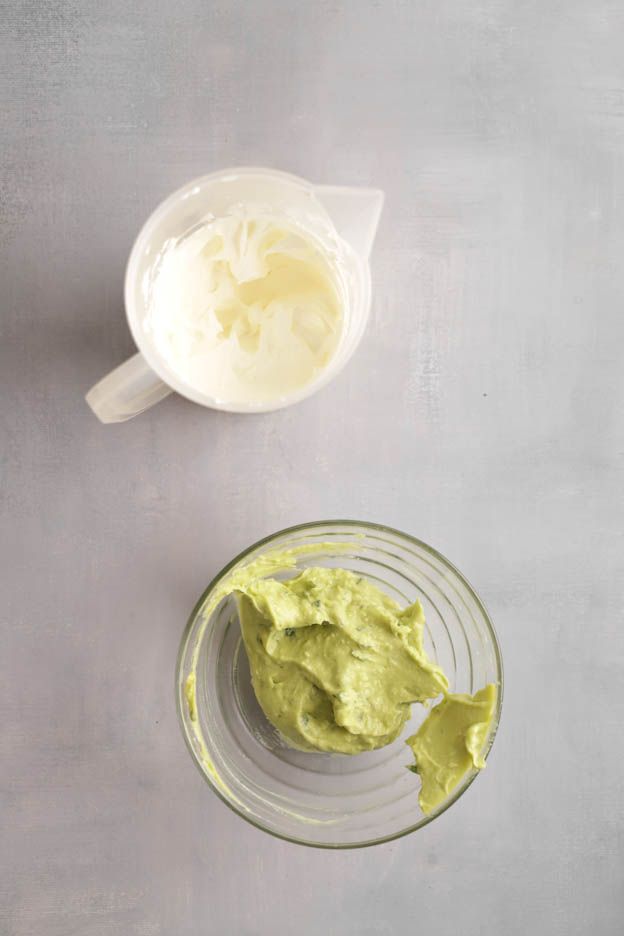 Whipped cream in a jug beside avocado cream in a glass bowl before folding together
