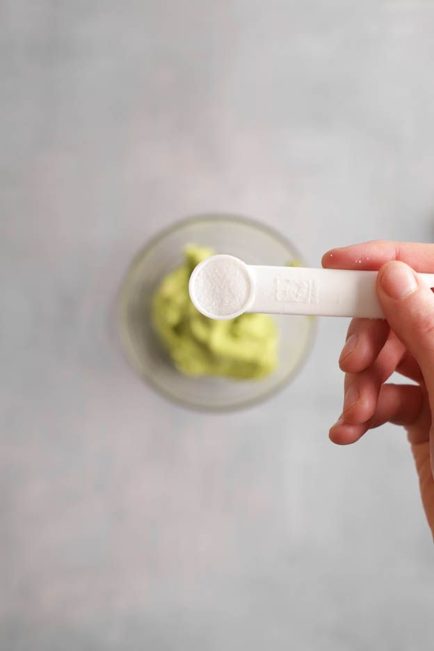 Measuring spoon above a bowl of avocado purée while dosing the seasoning