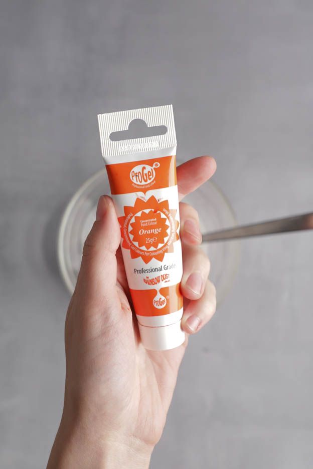 Une main tient un tube de colorant alimentaire en gel orange au-dessus du Bol