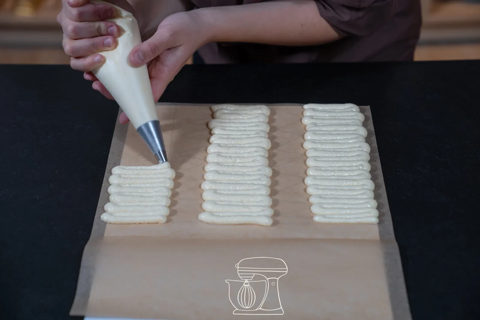 Piping bag forming a zigzag strip of sponge mixture on baking paper, with a smoothed sponge surface beside it