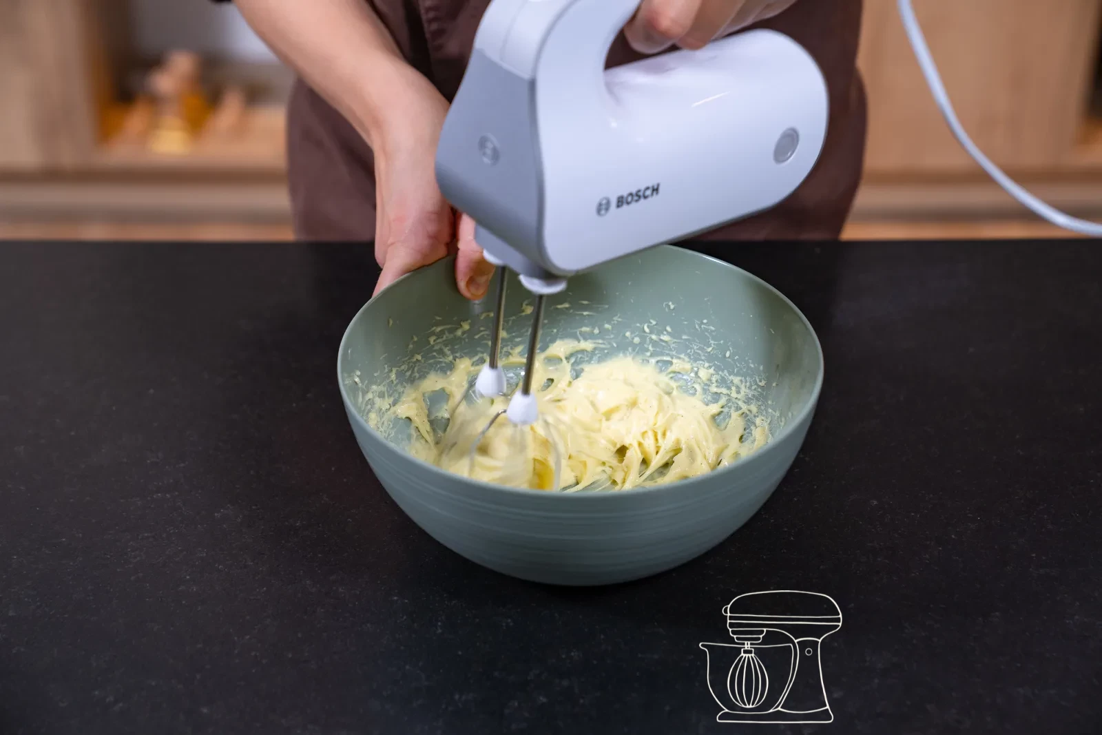 Thickened vanilla cream being stirred in the pot with a whisk, with a bowl and cling film beside it