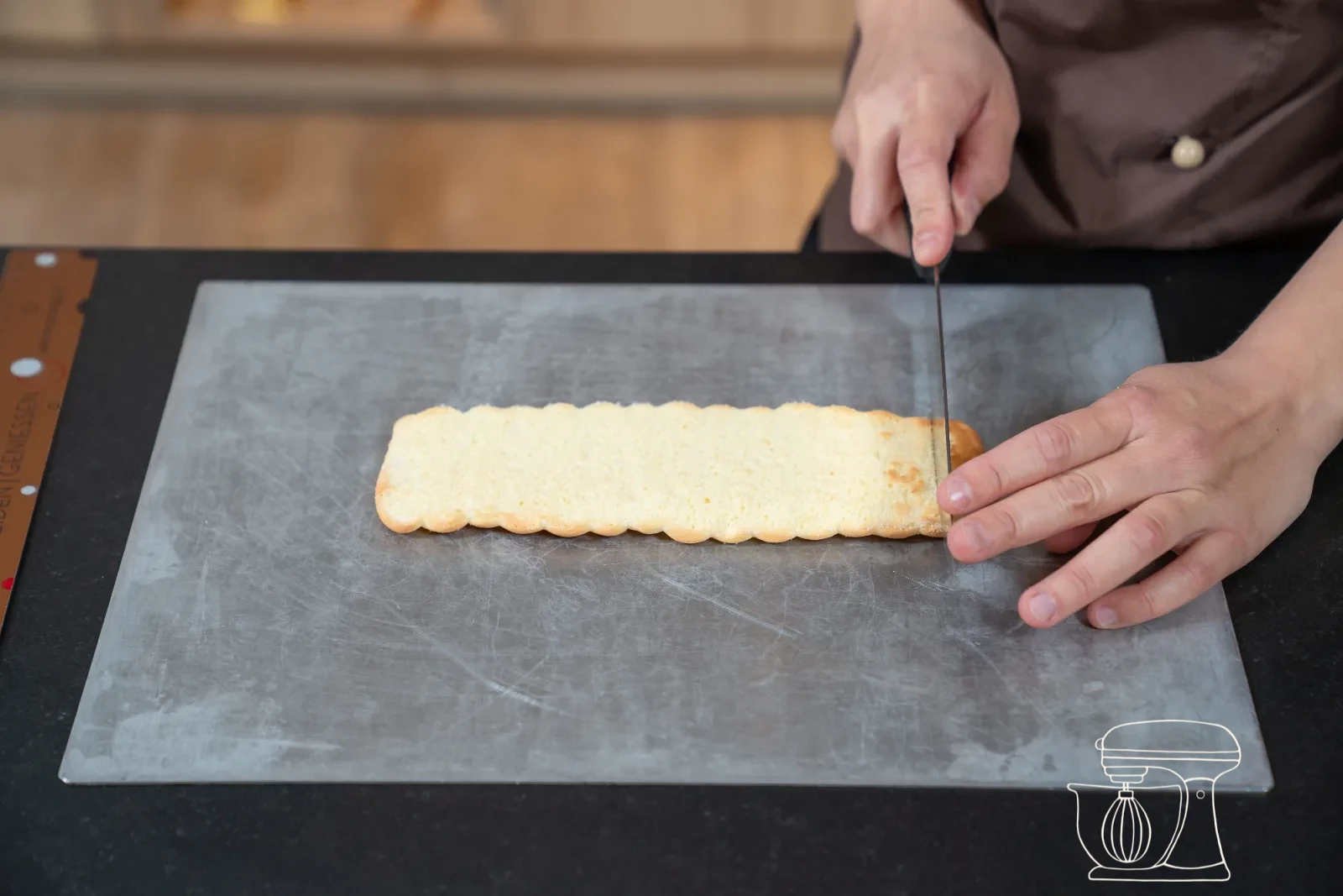 Trimmed sponge strip being set as a ring into a round patisserie mold, with cut-out sponge bases beside it