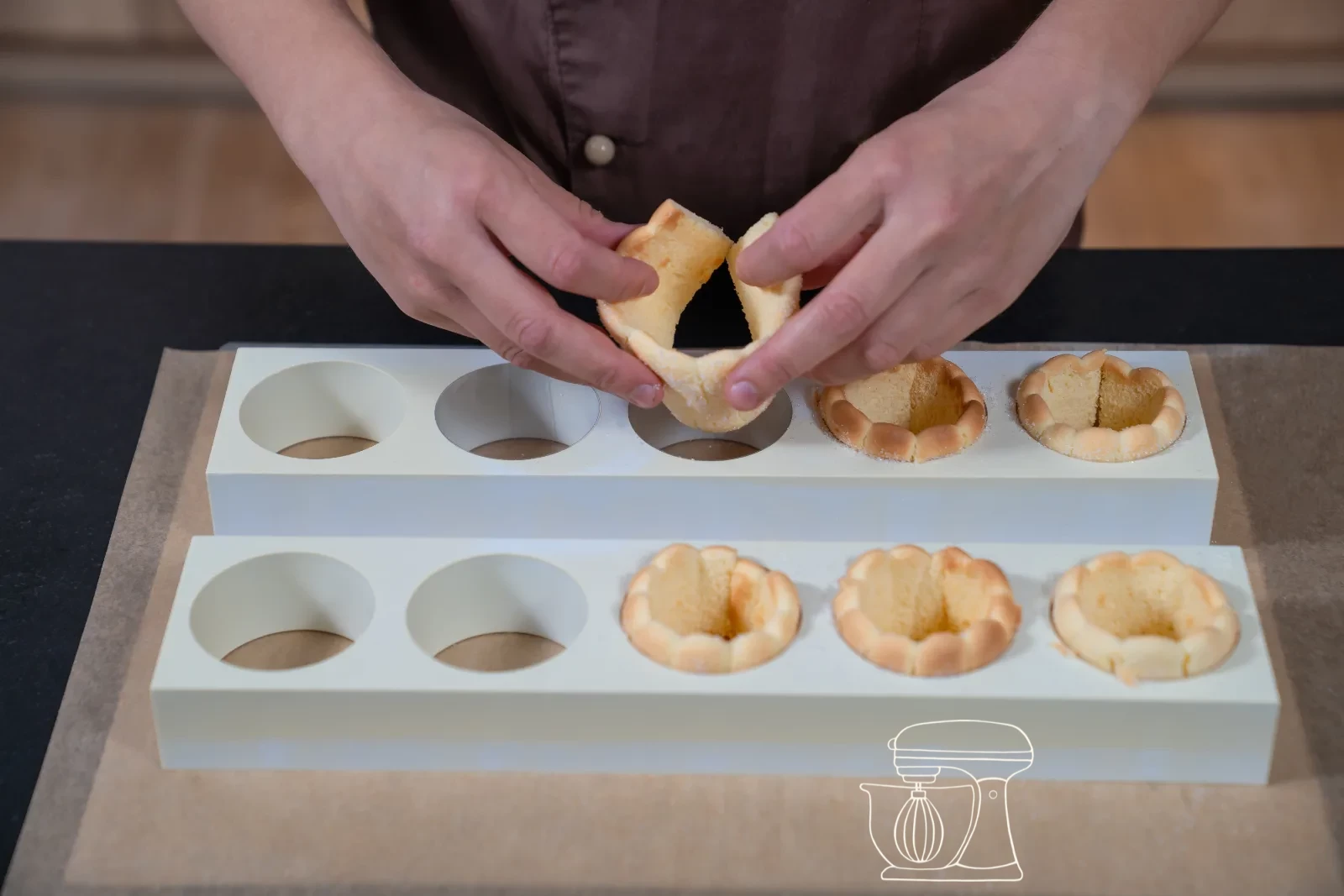 Trimmed sponge strip being set as a ring into a round patisserie mold, with cut-out sponge bases beside it