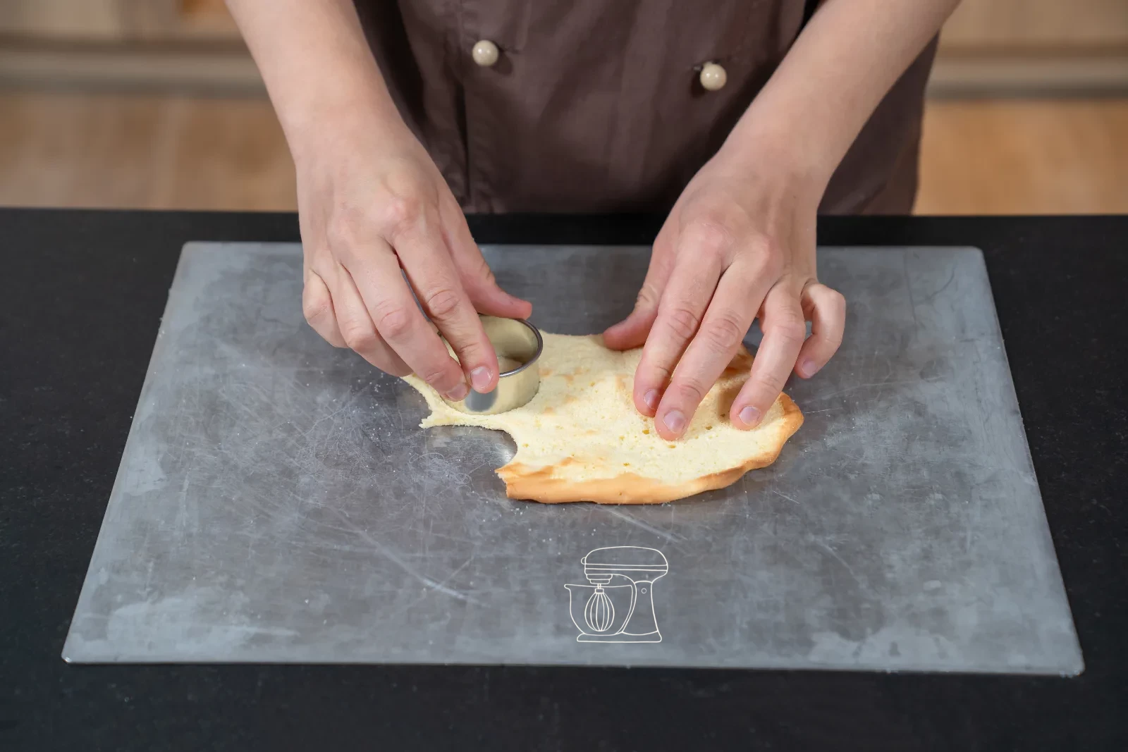 Trimmed sponge strip being set as a ring into a round patisserie mold, with cut-out sponge bases beside it