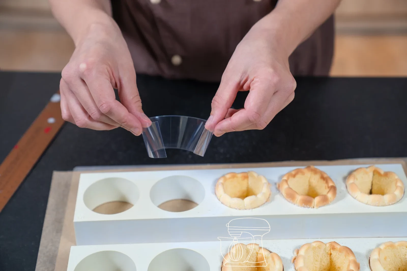 Trimmed sponge strip being set as a ring into a round patisserie mold, with cut-out sponge bases beside it