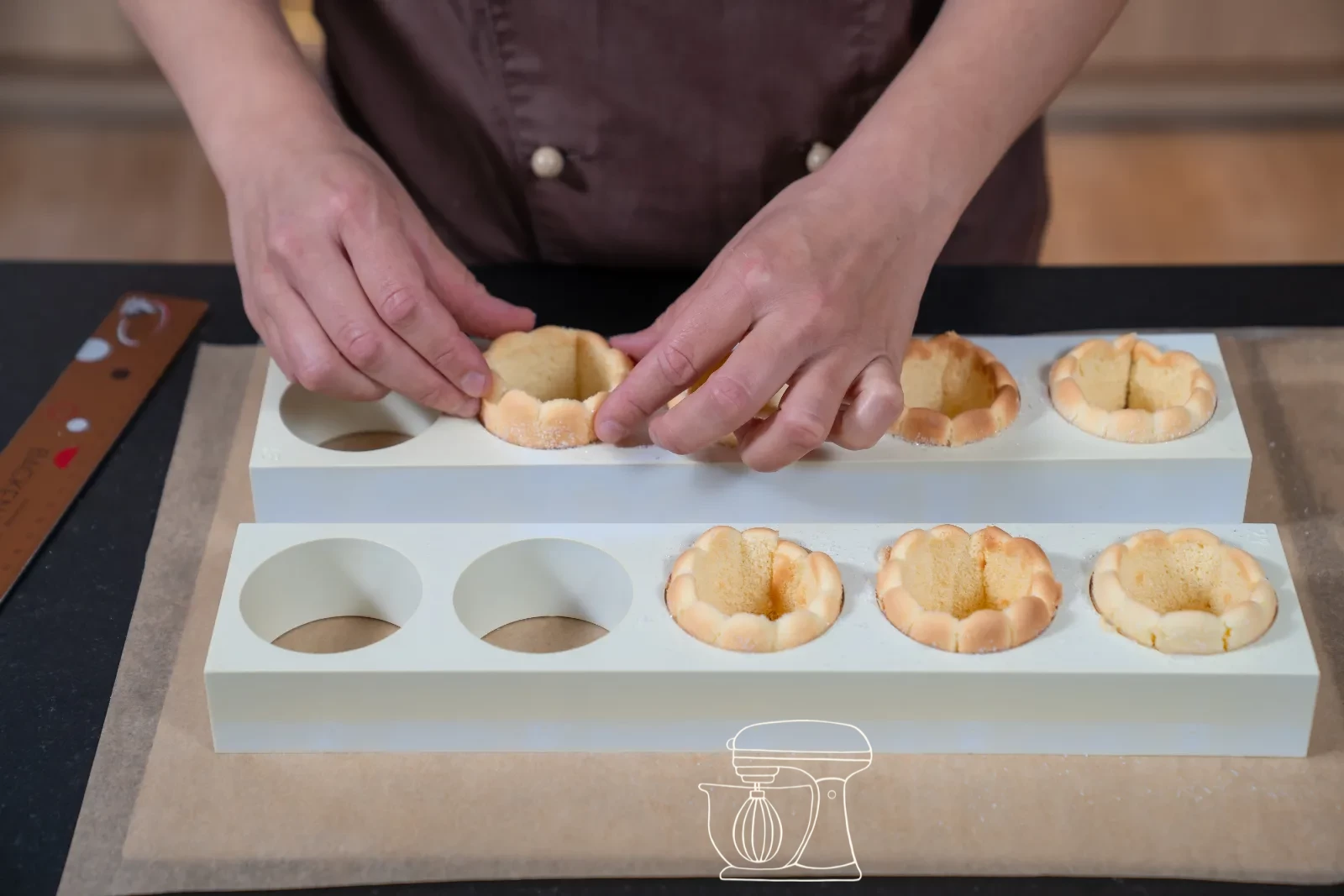 Trimmed sponge strip being set as a ring into a round patisserie mold, with cut-out sponge bases beside it