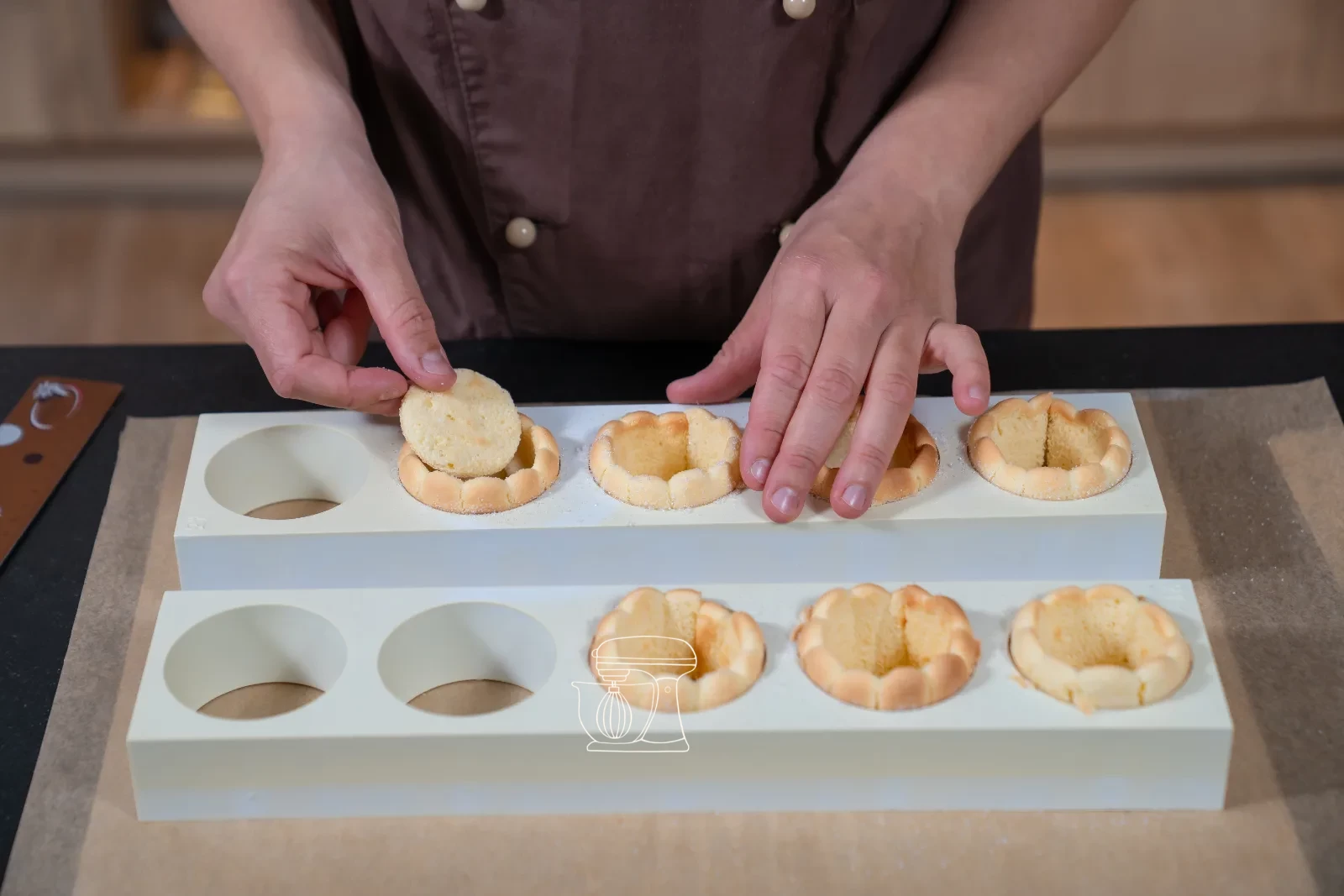 Trimmed sponge strip being set as a ring into a round patisserie mold, with cut-out sponge bases beside it