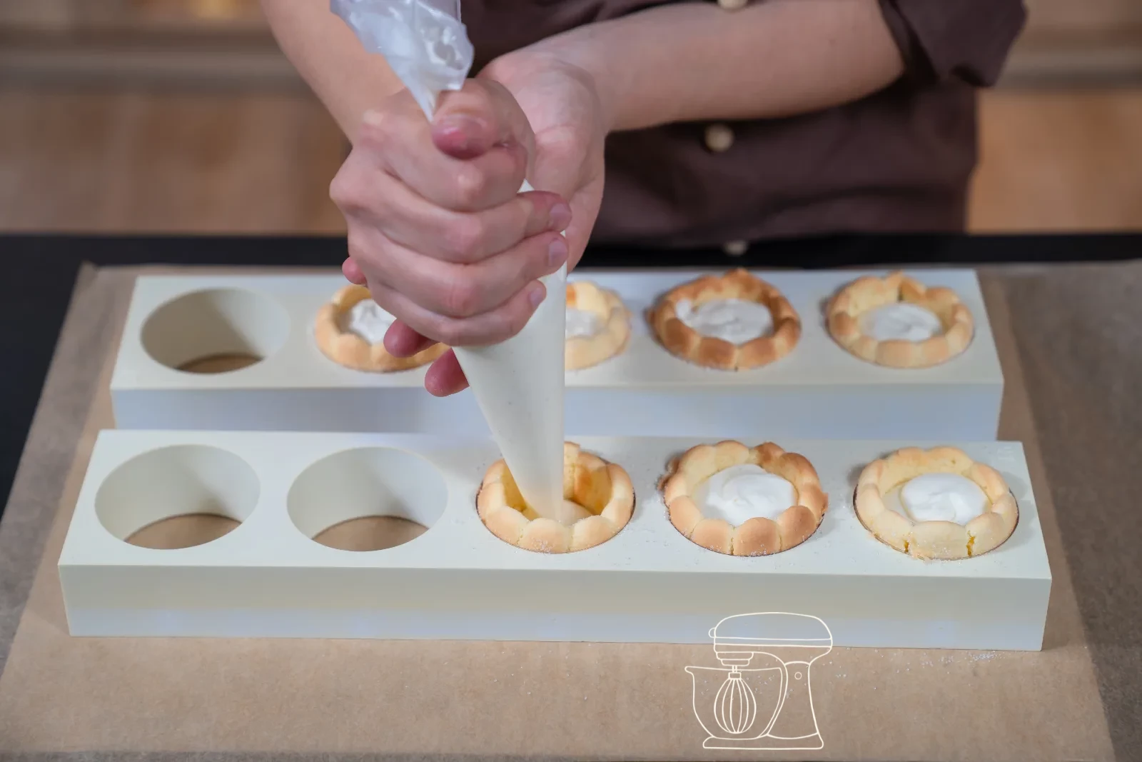 Vanilla cream being piped as a rosette onto a filled mini charlotte, with fresh berries and icing sugar in the background