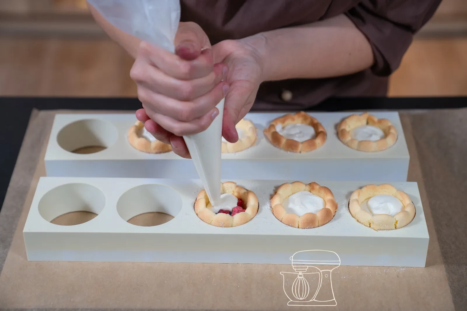 Vanilla cream being piped as a rosette onto a filled mini charlotte, with fresh berries and icing sugar in the background