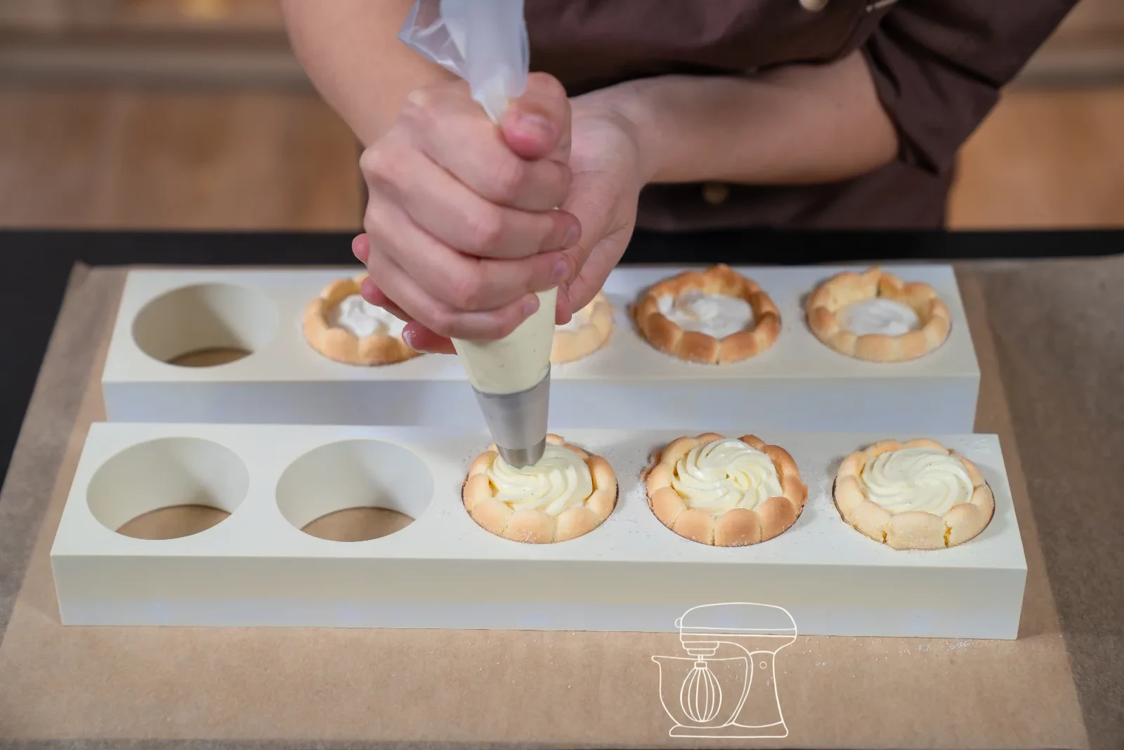 Vanilla cream being piped as a rosette onto a filled mini charlotte, with fresh berries and icing sugar in the background