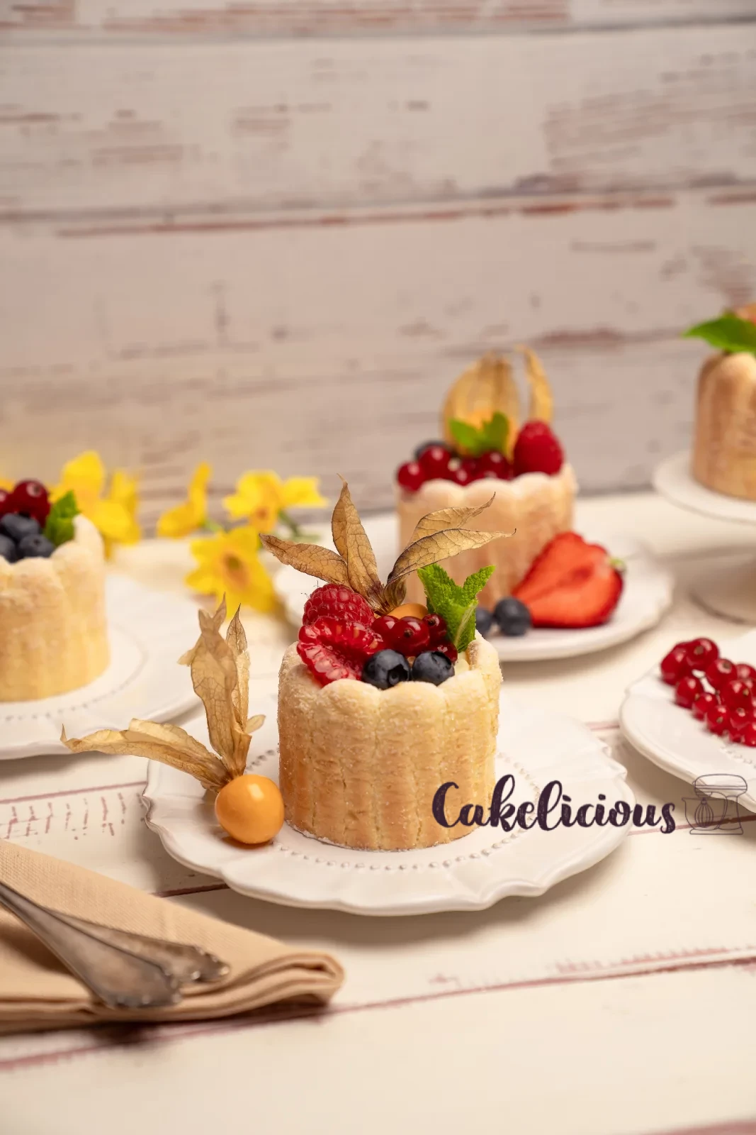 Row of finished charlottes on a stand, with a bowl of mixed berries in the background