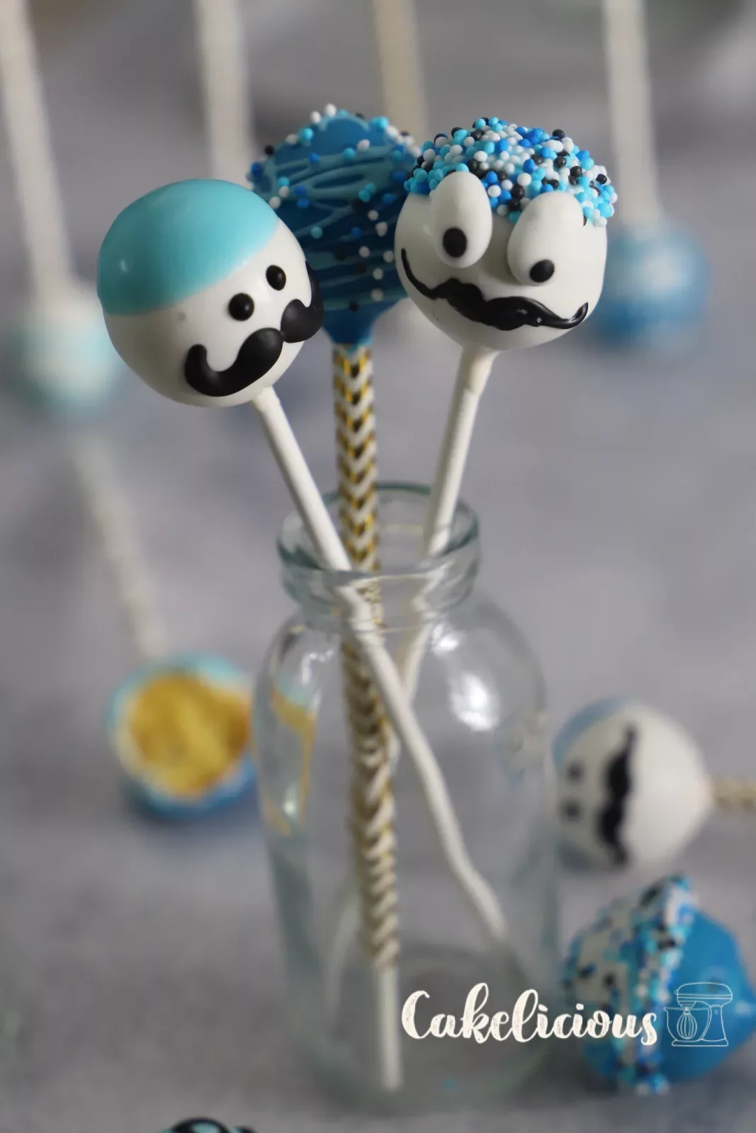 Drei Cake Pops mit Schnurrbart und blauen Zuckerperlen in einer Glasflasche