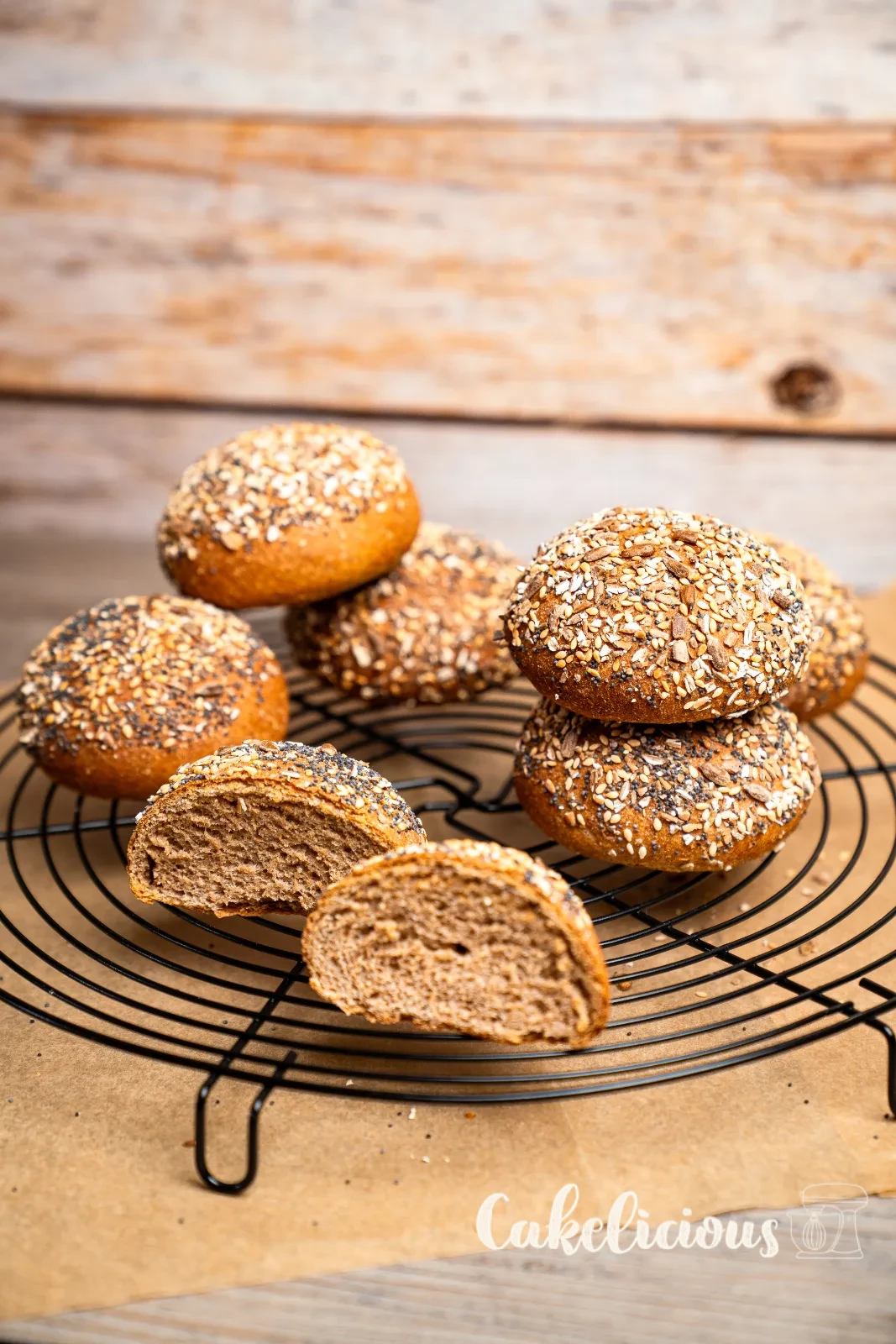 Panini integrali di farro con crosta di semi impilati su una tavola di legno, uno tagliato