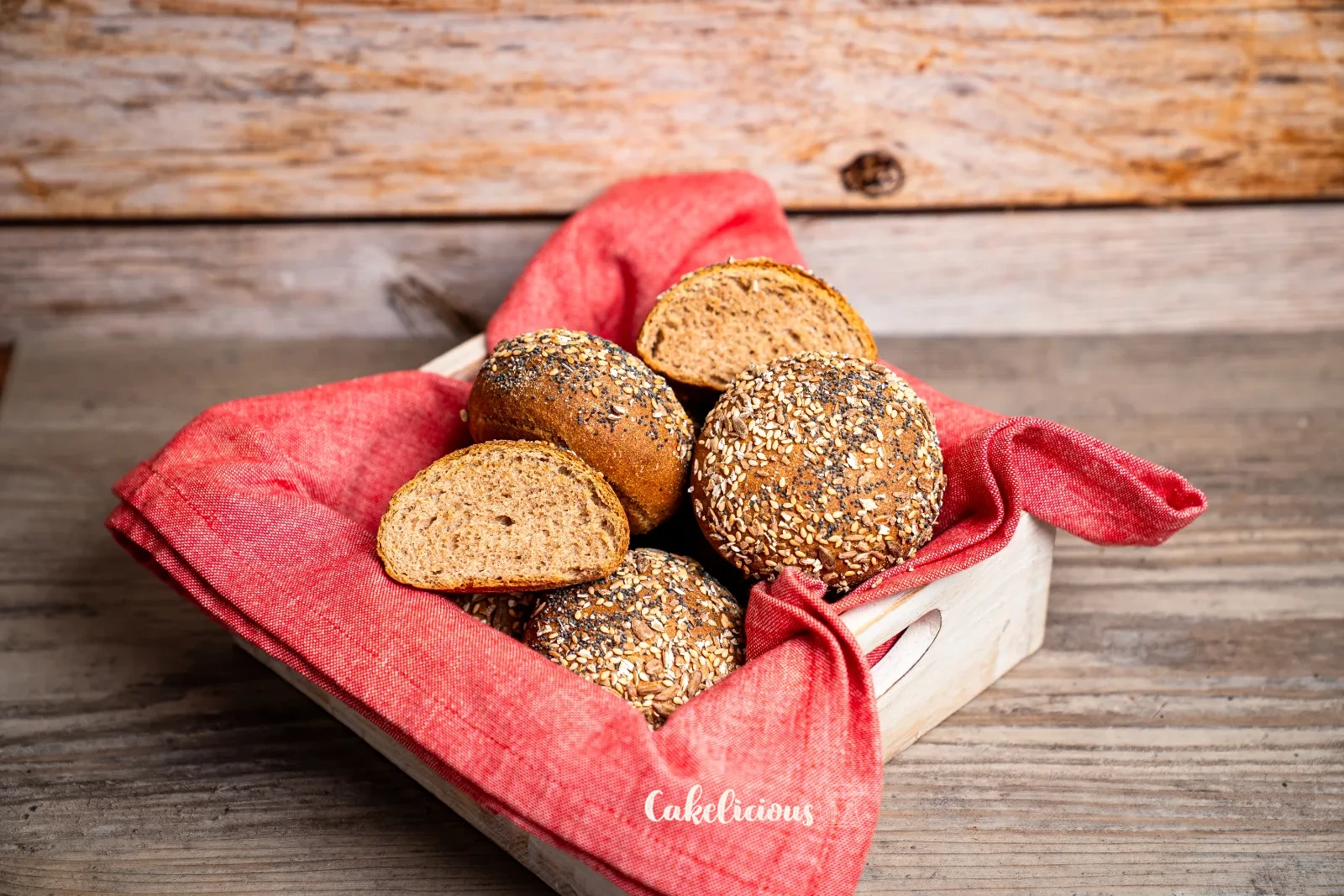 Panini integrali di farro con crosta di semi impilati su una tavola di legno, uno tagliato