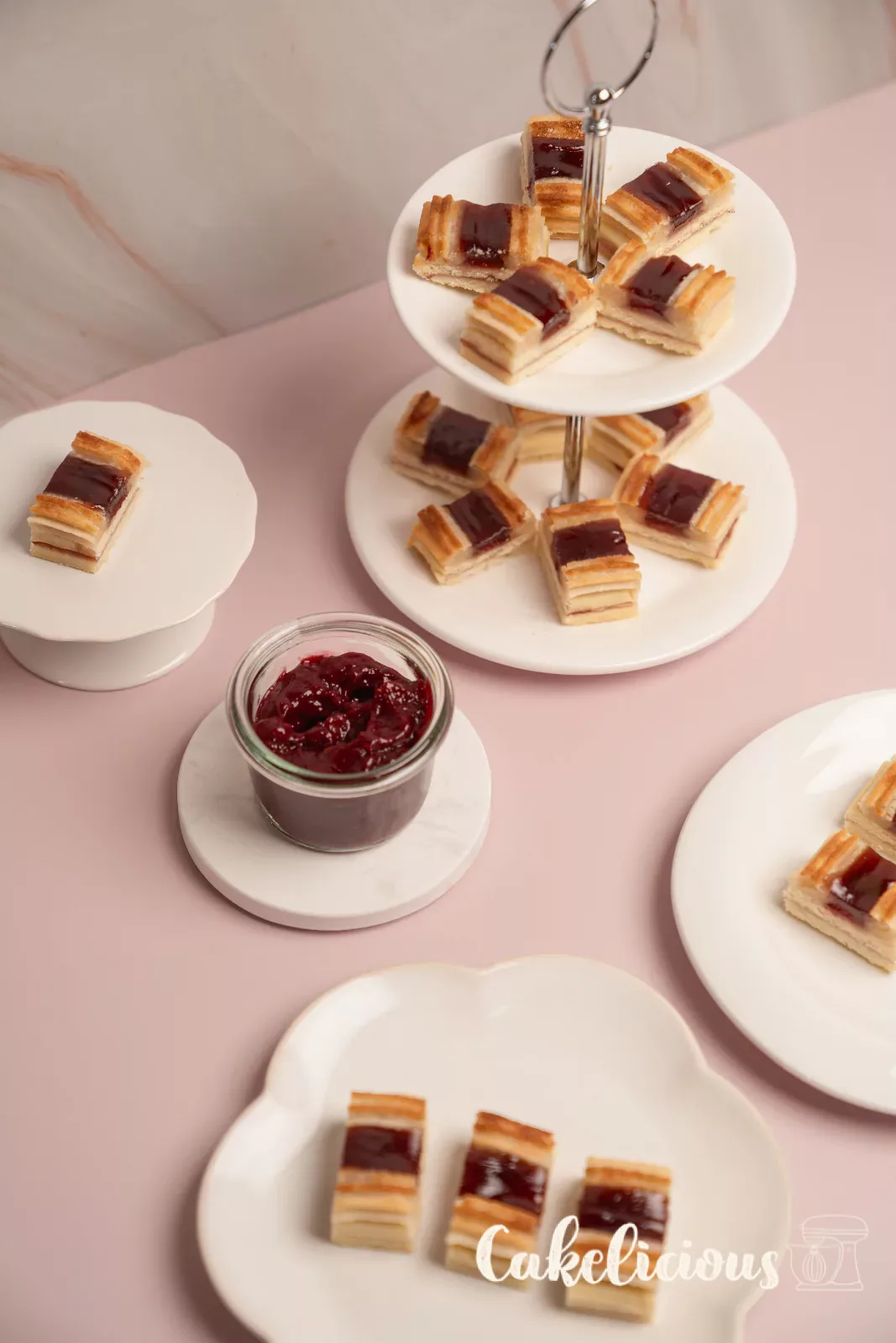 Tower of railway worker cookies in front of a wooden wall, with raspberry jam in a jar and a spoonful of jam