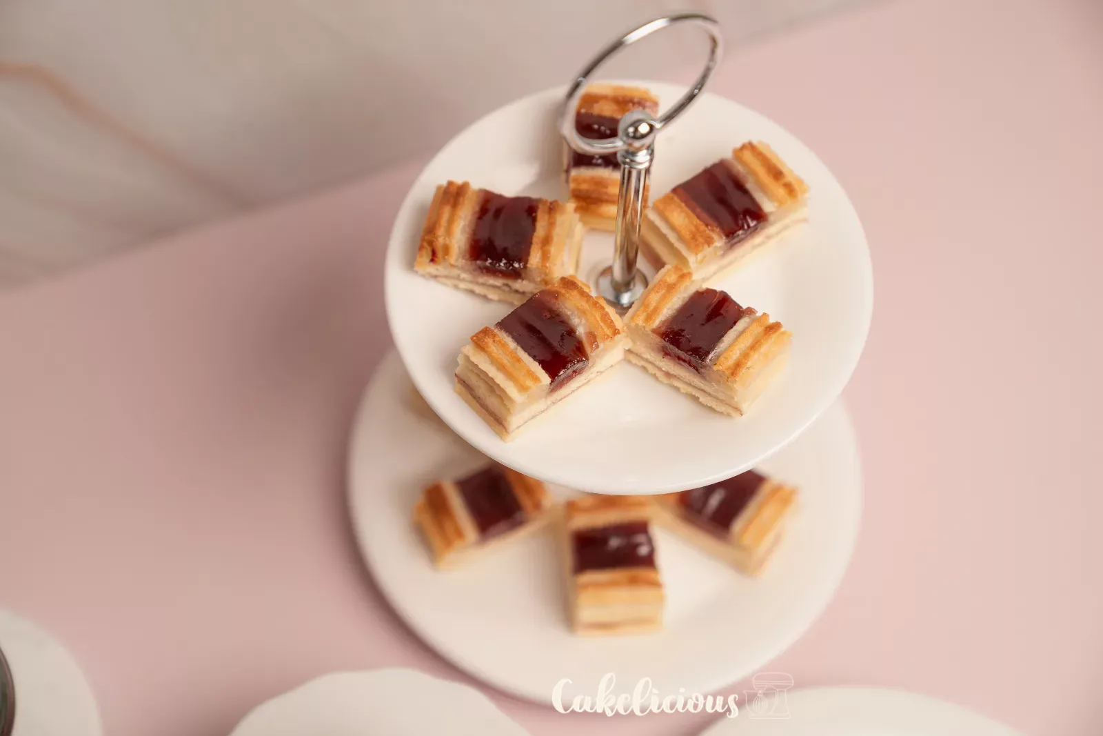 Railway worker cookies with almond rails and raspberry jam in front of light marble, with a spoonful of jam beside them