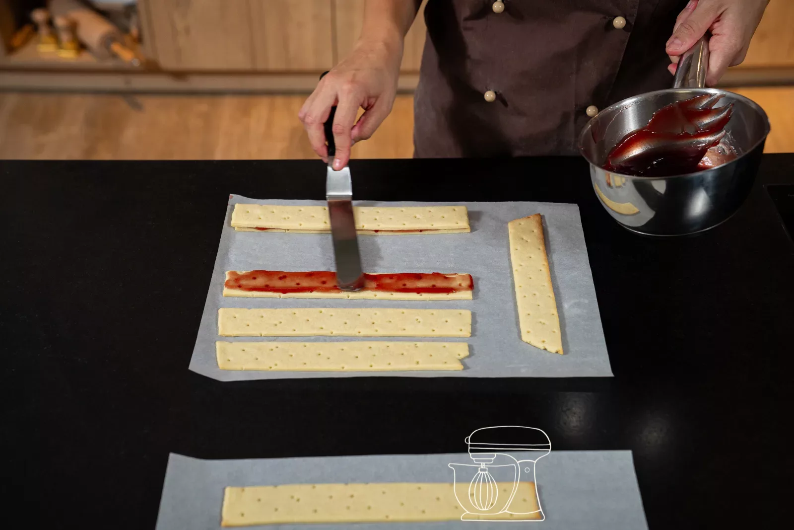 Warm raspberry jam being spread thinly onto a dough strip with an angled palette