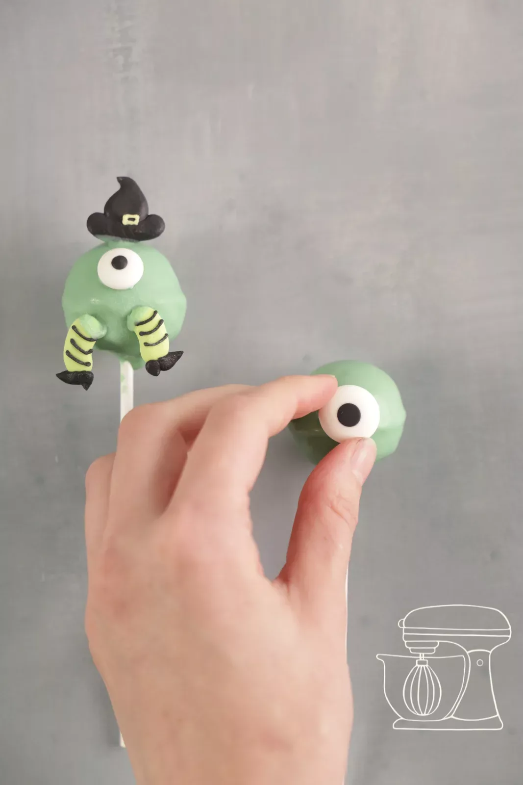 Candy eye being stuck onto a green cake pop