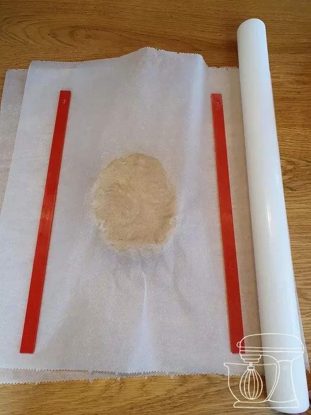 Dough being rolled out to 3 mm thin between baking paper with rolling guides