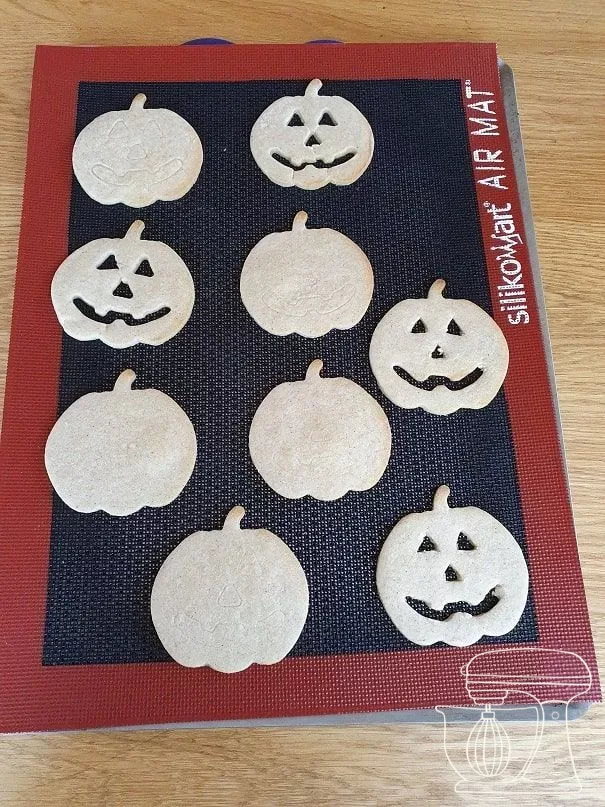 Pumpkin cookies on a perforated baking tray with a perforated mat
