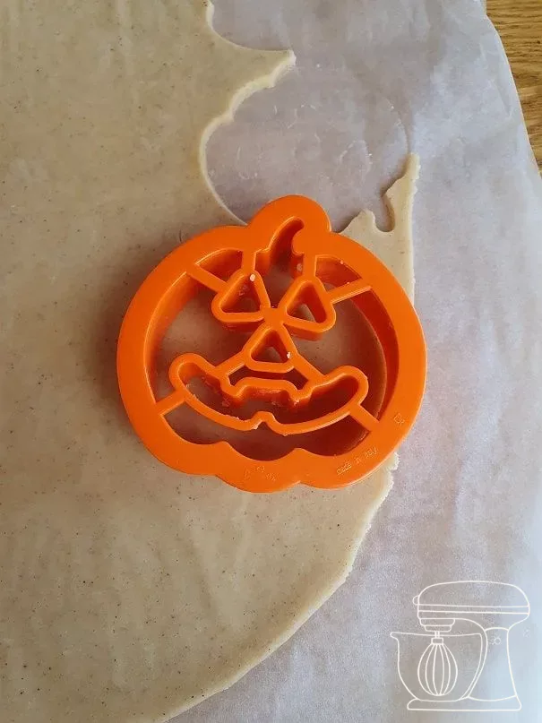 Pumpkin cookie cutter being pressed lightly into the chilled dough