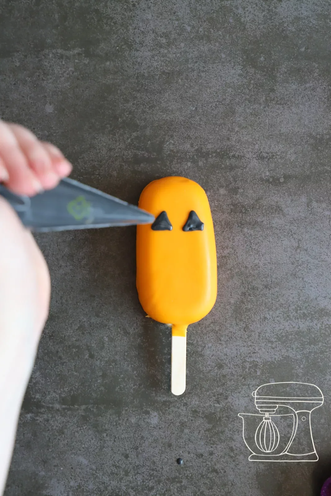 Triangle eyes being piped onto an orange cakesicle