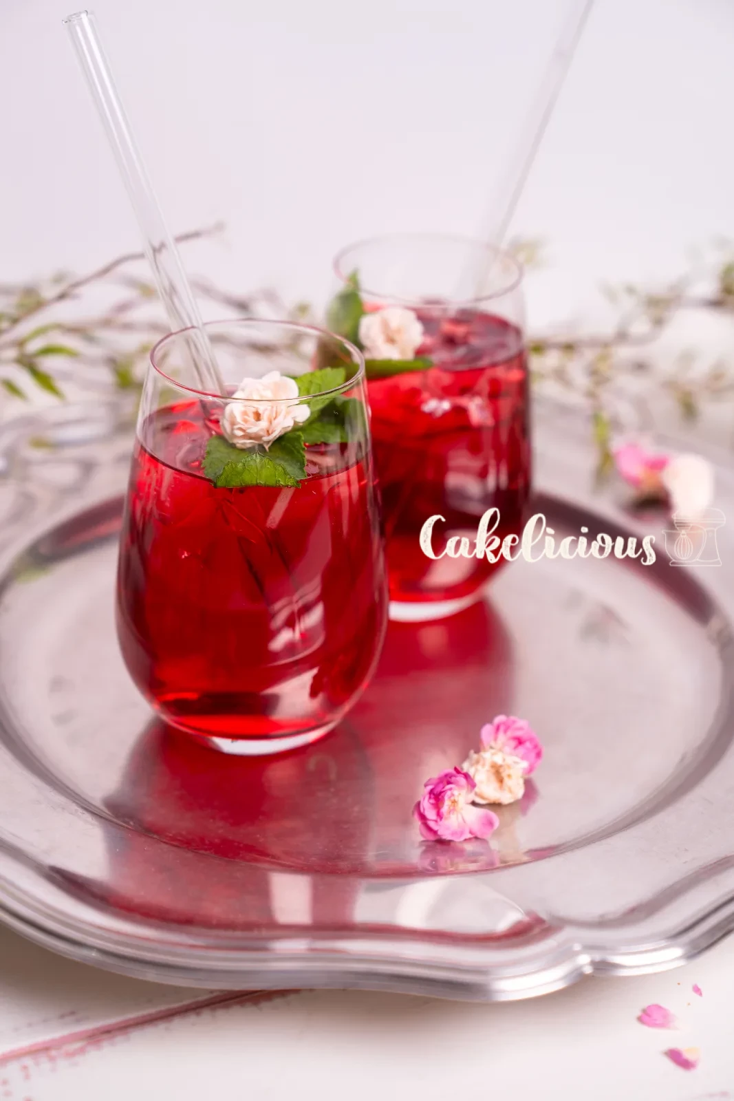Un bicchiere di tè freddo all'ibisco con cannuccia di vetro, foglia di menta e petalo di rosa essiccato