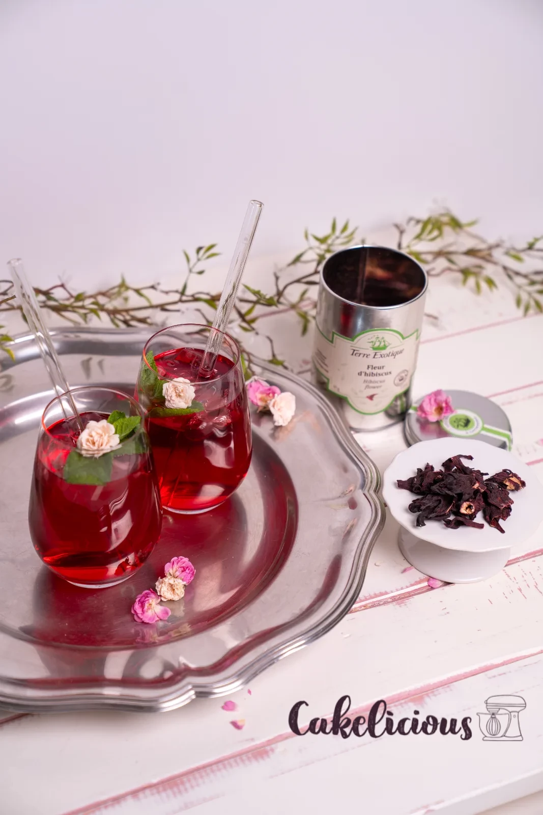 Un bicchiere di tè freddo all'ibisco con cannuccia di vetro, foglia di menta e petalo di rosa essiccato