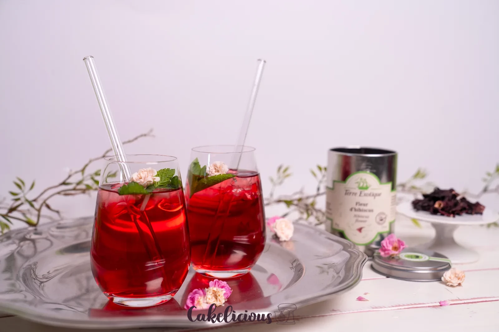 Un bicchiere di tè freddo all'ibisco con cannuccia di vetro, foglia di menta e petalo di rosa essiccato