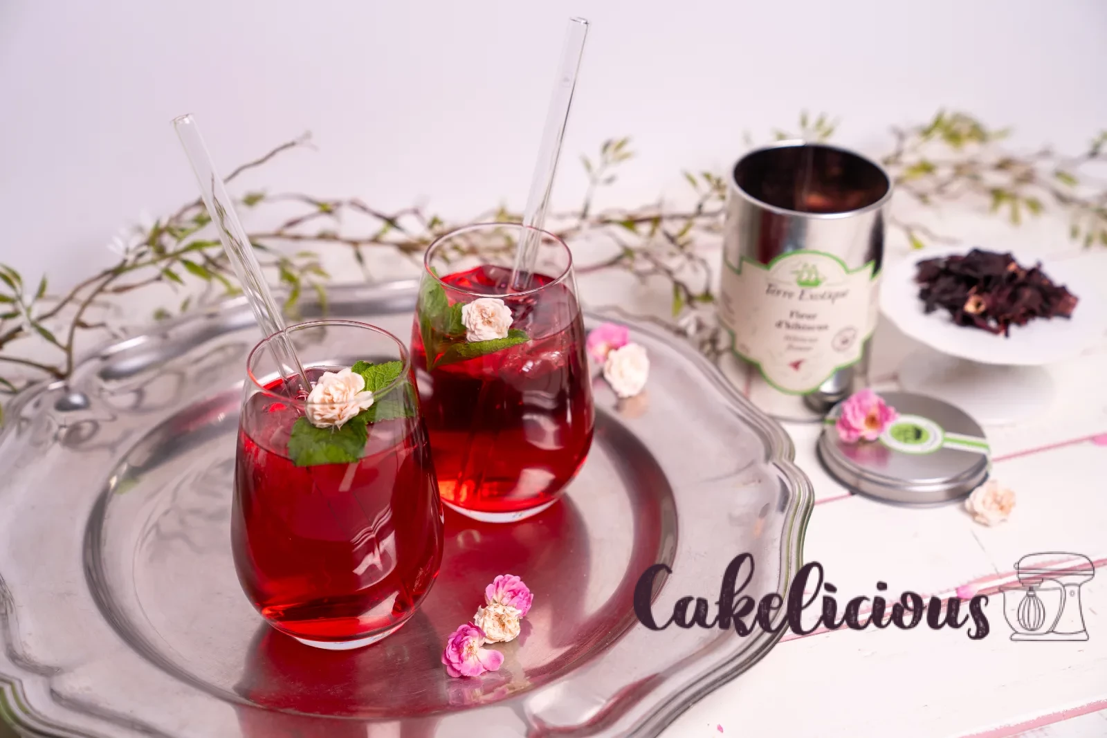 Un bicchiere di tè freddo all'ibisco con cannuccia di vetro, foglia di menta e petalo di rosa essiccato