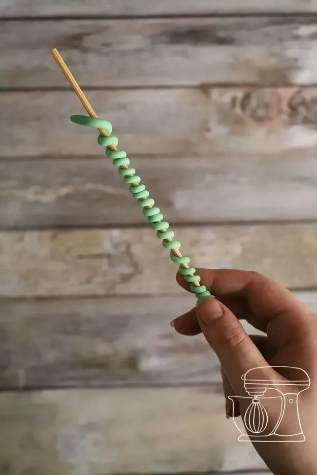 Strand of Modeling chocolate being rolled around a wooden stick