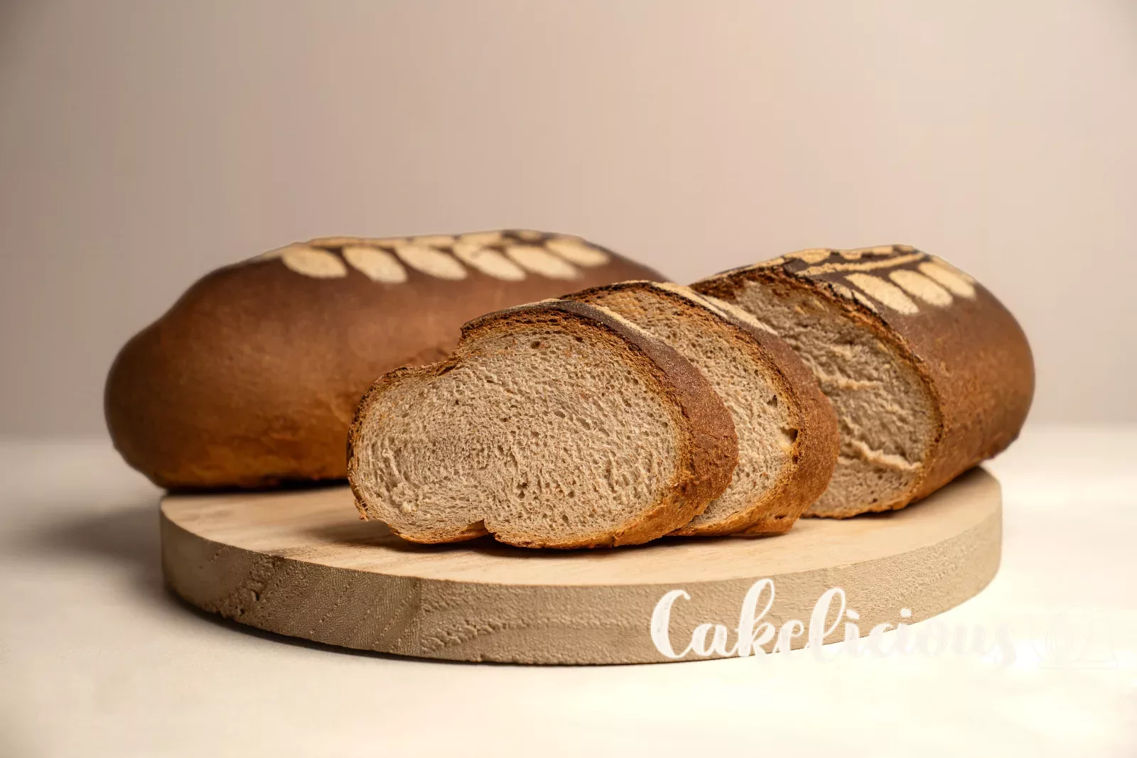Pane rustico tagliato con mollica morbida, accanto un pane intero con motivo a spiga su un tagliere di legno