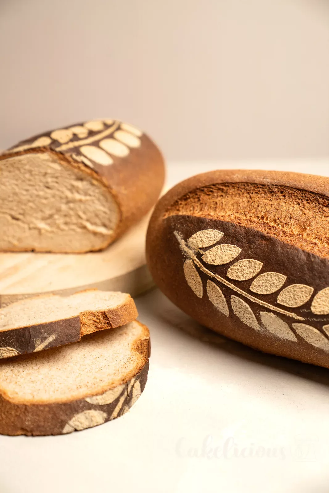 Pane rustico tagliato con mollica soffice, accanto un pane intero con motivo a spiga su un tagliere di legno