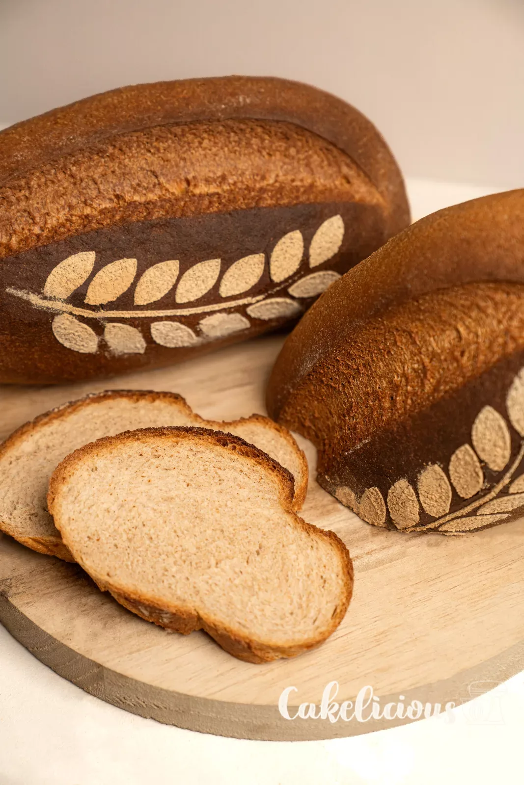 Pane rustico tagliato con mollica soffice, accanto un pane intero con motivo a spiga su un tagliere di legno