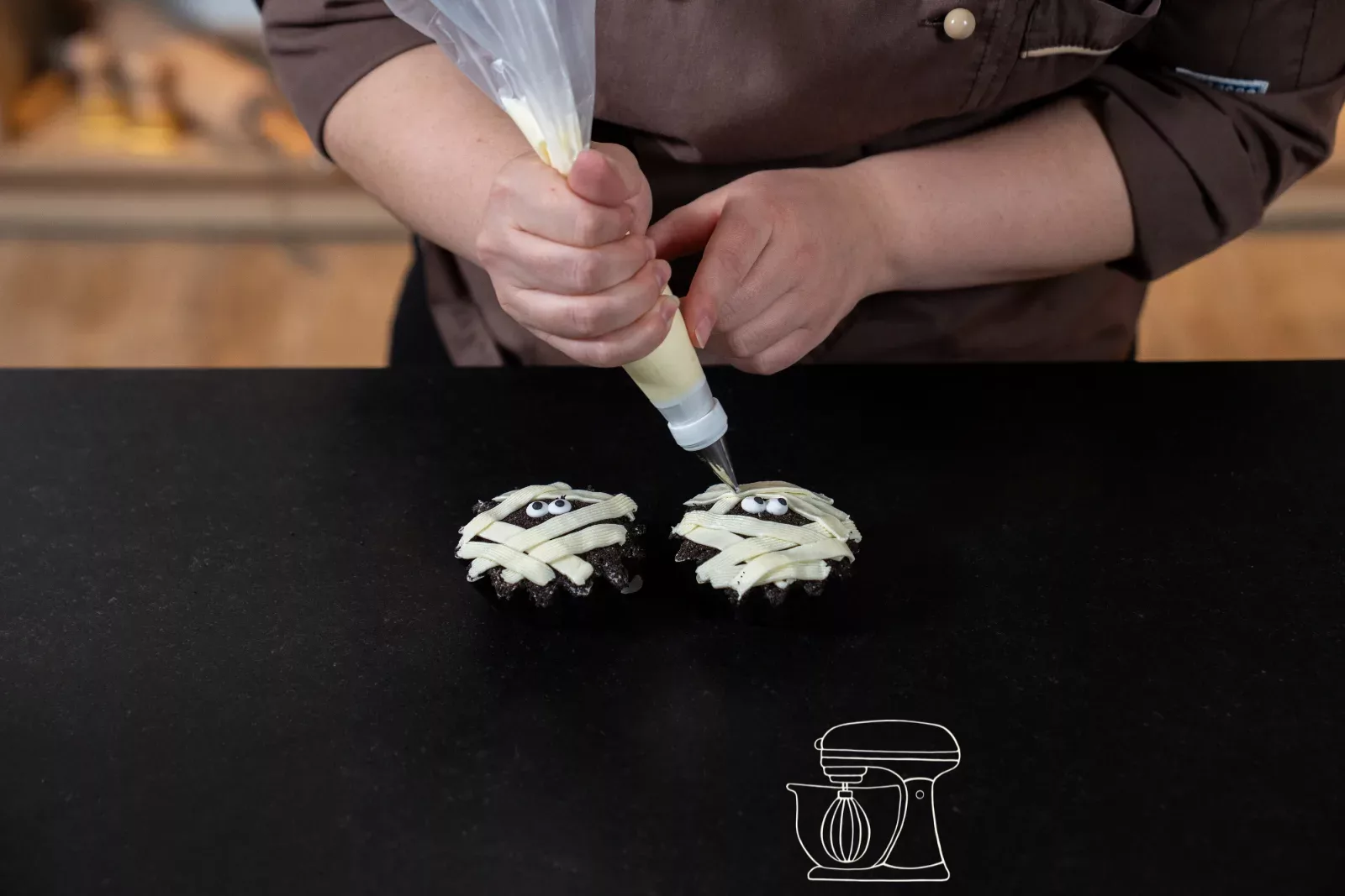Weisses Frosting wird als Bandagen über den mit Oreo-Bröseln bedeckten Cupcake gespritzt