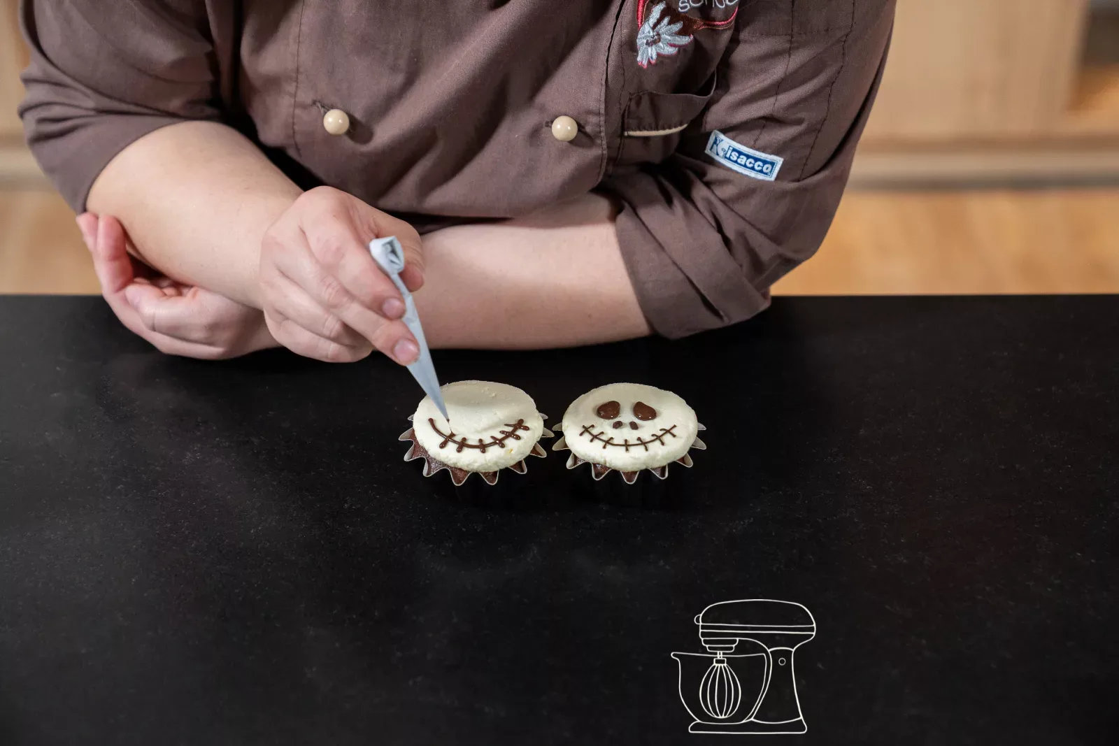 Gesicht wird mit dunkler Kuchenglasur auf das weisse Frosting gemalt