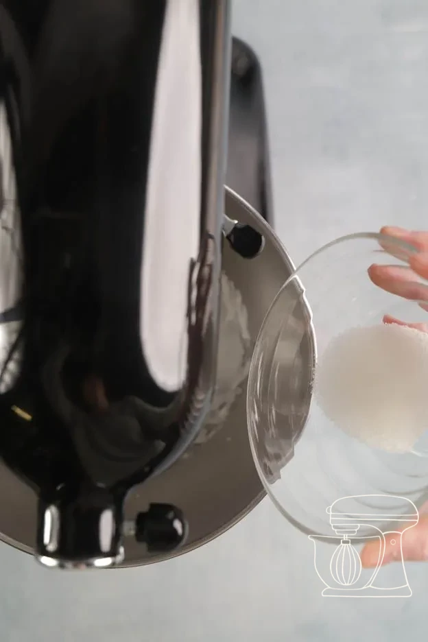 Sugar being added spoonful by spoonful into the foamy egg white mixture