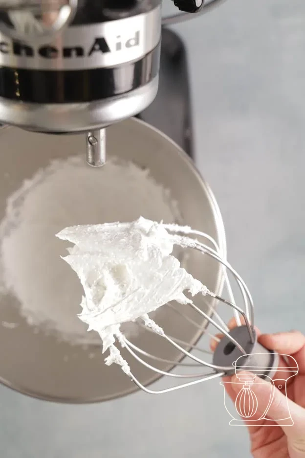 Sugar being added spoonful by spoonful into the foamy egg white mixture